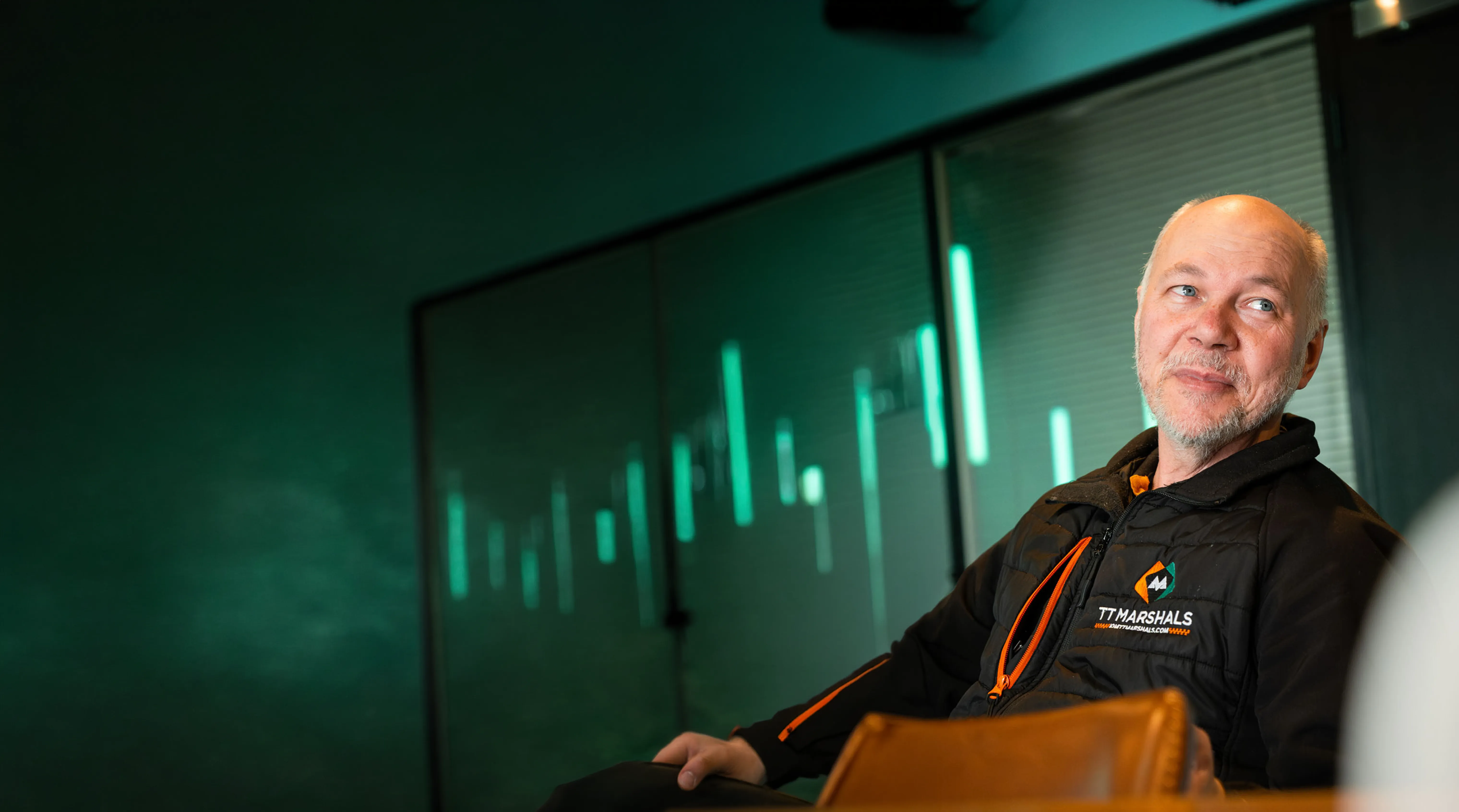 Andy Williams of TT Marshals in the Dot Performance offices with teal background.